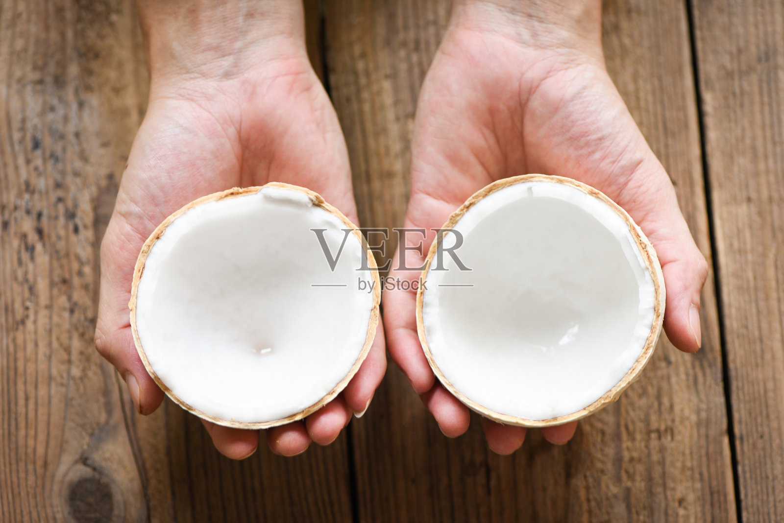将椰子切成一半在手，新鲜椰子放在旧木桌上做食物。照片摄影图片