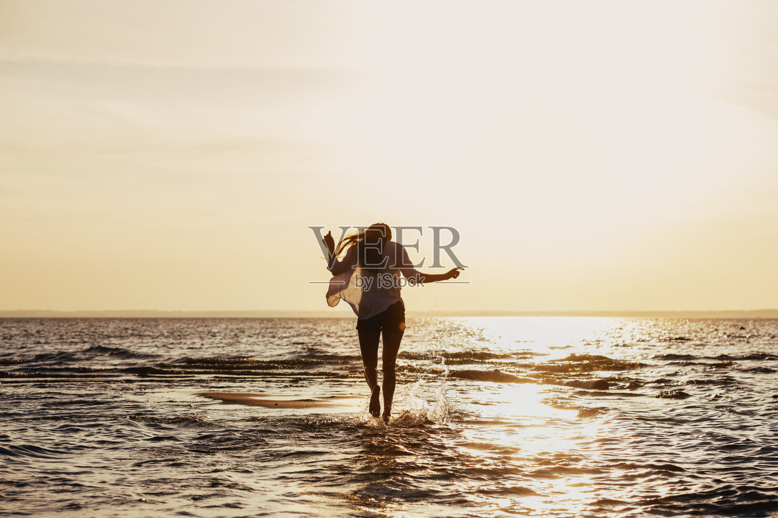 苗条的女孩走在日落海滩的水照片摄影图片