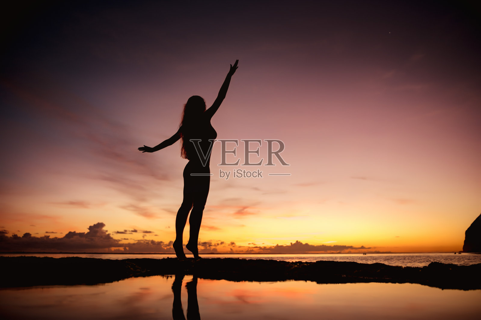 快乐的女人在日落海滩上举起手臂照片摄影图片