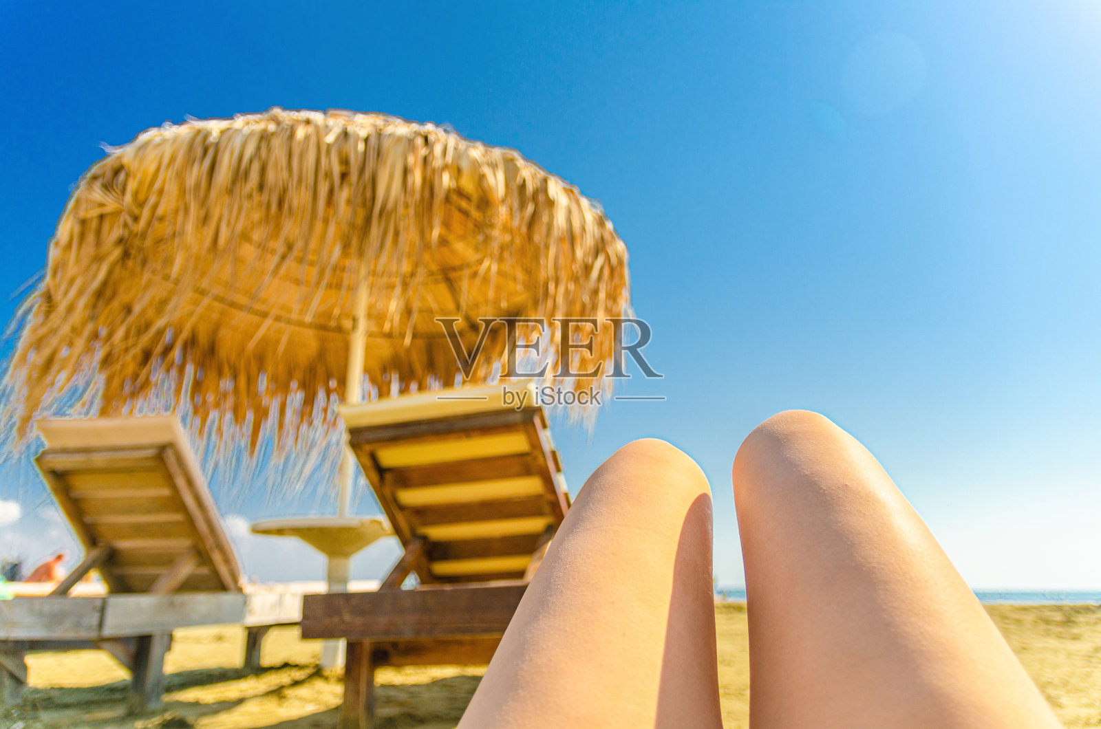 女人女孩腿日光浴在热带沙滩上模糊的稻草遮阳伞和木制太阳躺椅照片摄影图片