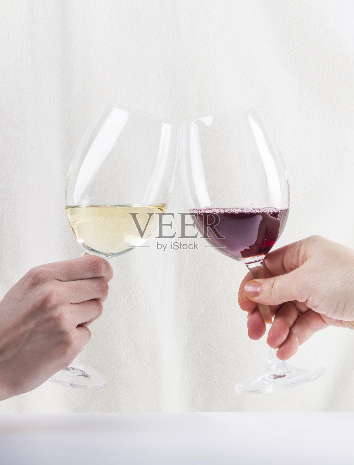 在白色人造毛皮的背景下，两个人碰杯红酒和白葡萄酒照片摄影图片