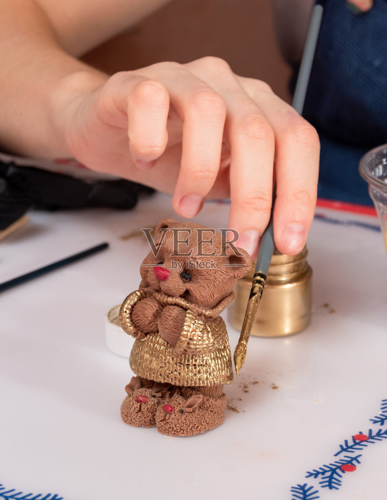 一个男人的手，用画笔在一个巧克力形象的小熊幼崽上涂金色的油漆。有选择性的重点。照片摄影图片