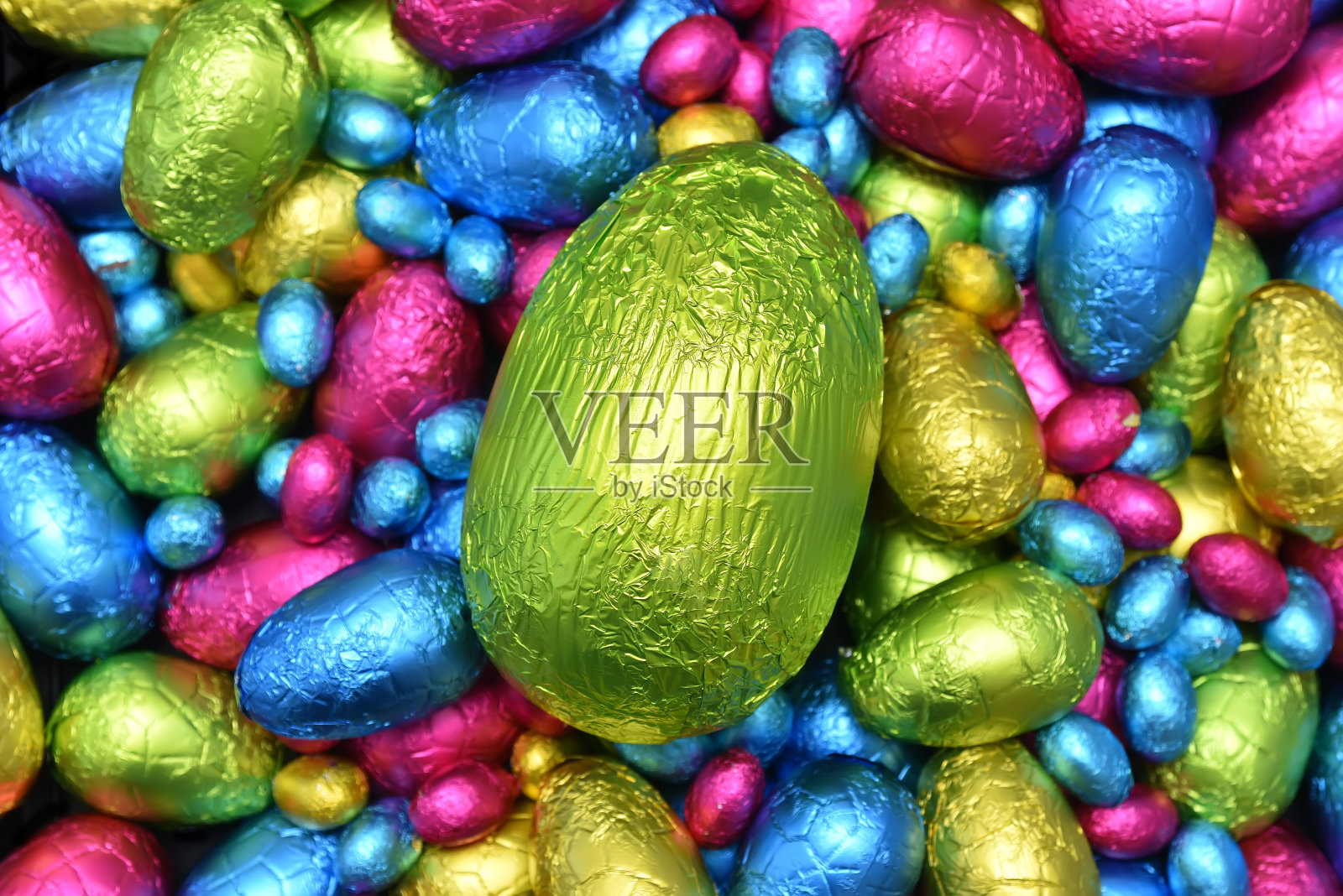 1 .用锡箔纸包裹一堆或一组颜色各异、大小各异的巧克力复活节彩蛋，彩蛋的颜色有粉色、蓝色、黄色和酸橙绿，中间放一个绿色的大鸡蛋。照片摄影图片