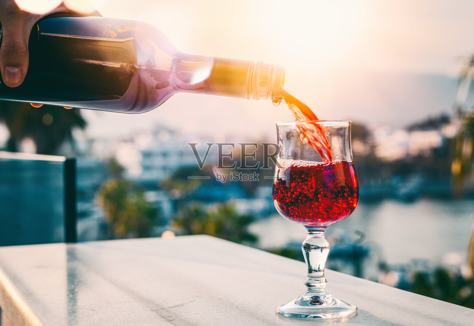 在一个日落城市的背景下，红酒从瓶子里倒进玻璃杯，休息和喝照片摄影图片