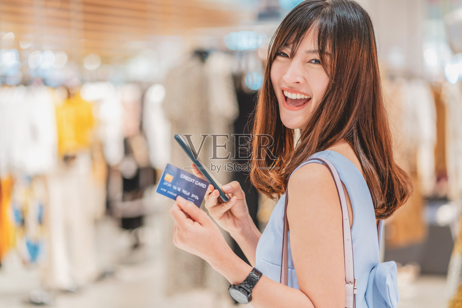 亚洲妇女使用信用卡与手机在百货商店网上购物的服装店背景，技术钱钱包和网上支付概念，信用卡模型照片摄影图片