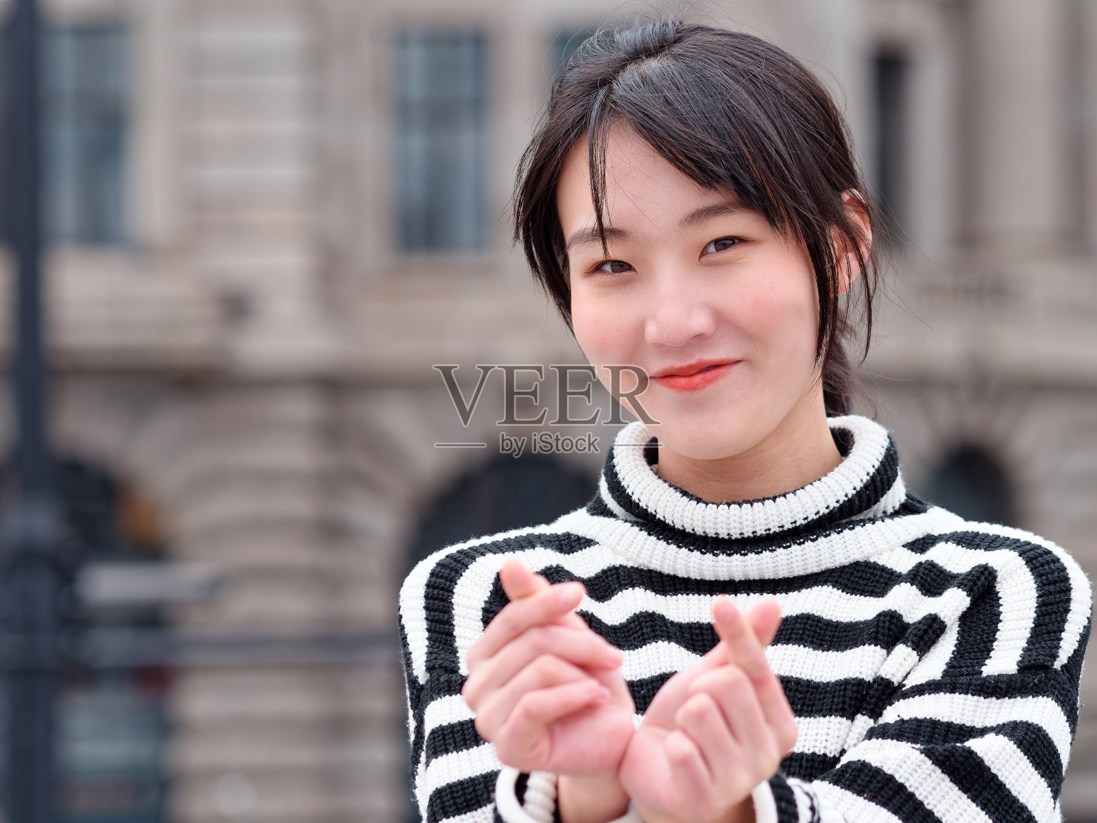 年轻的中国女人在镜头前微笑着用爱你的手势，快乐的女孩与城市建筑背景在上海的肖像。照片摄影图片