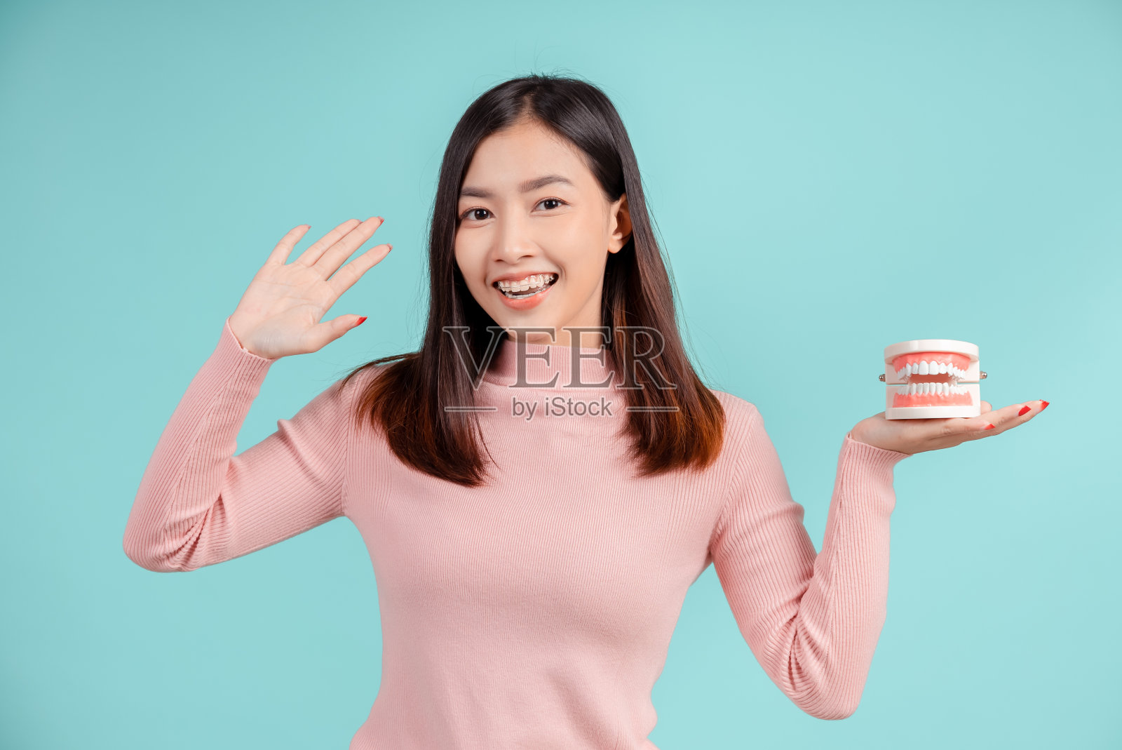 牙齿的亚洲妇女与牙齿样本和白色的牙齿增加信心为健康的蓝色背景孤立工作室拍摄，幸福的青少年微笑的面部表情。照片摄影图片