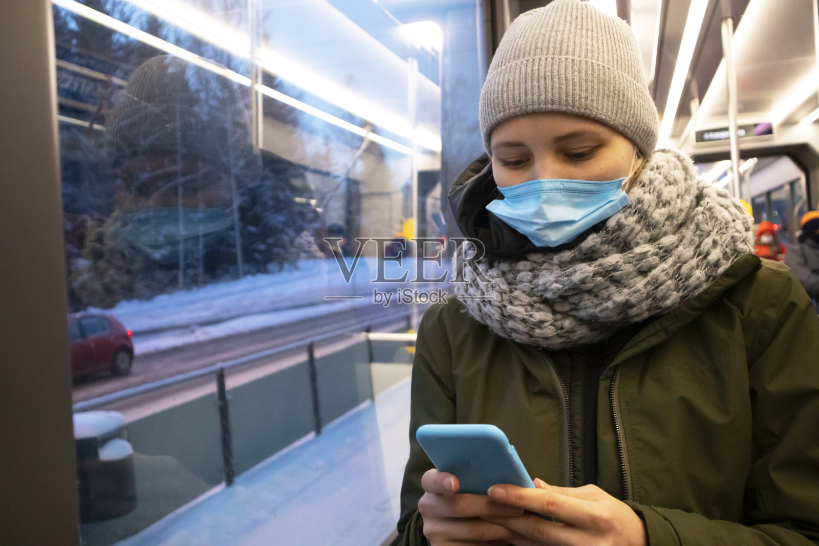 一名忧心忡忡的女性在公交车上戴着保护面罩，并使用智能手机照片摄影图片
