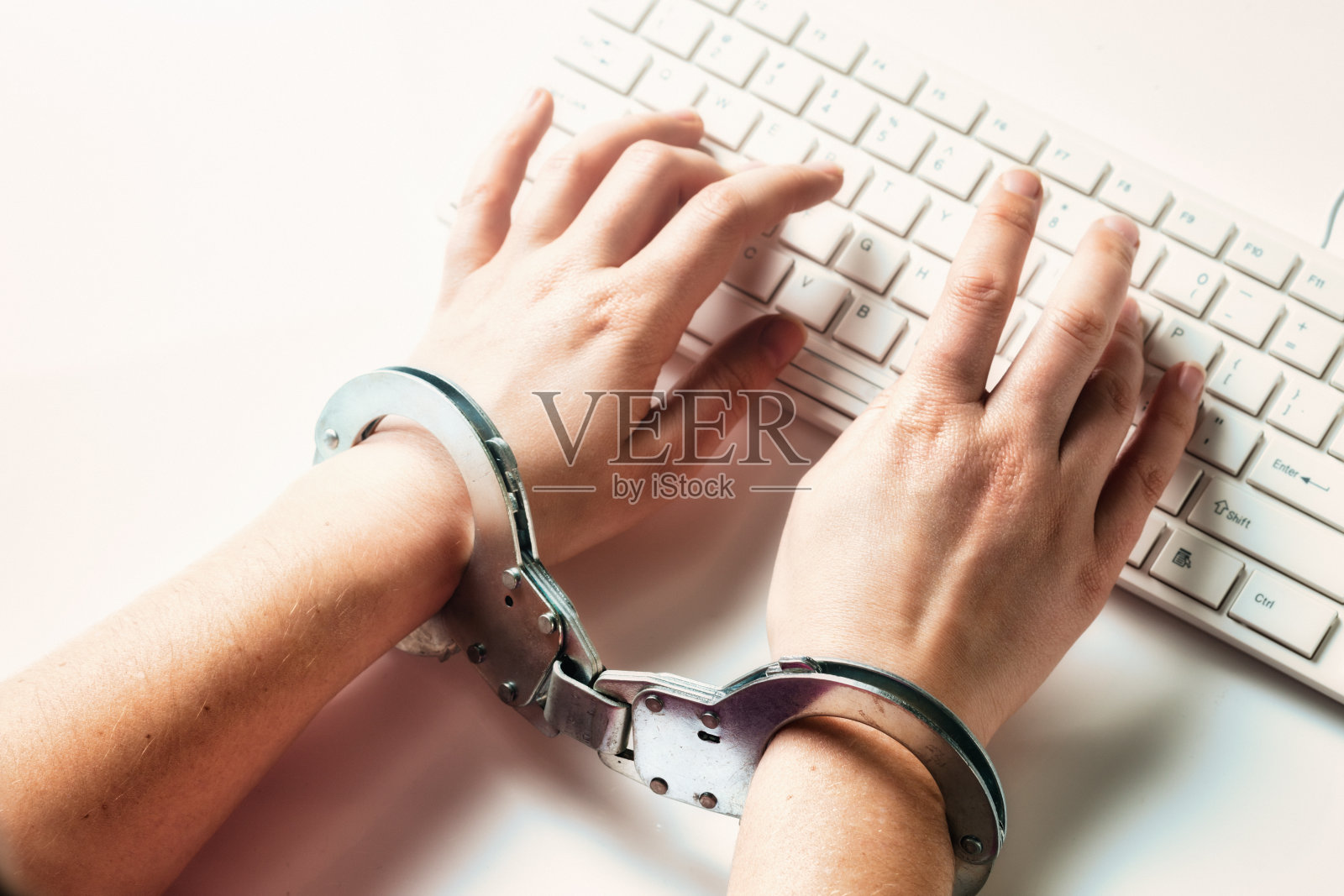 戴着手铐的妇女在电脑键盘前打字，象征着审查制度或被困在工作中照片摄影图片
