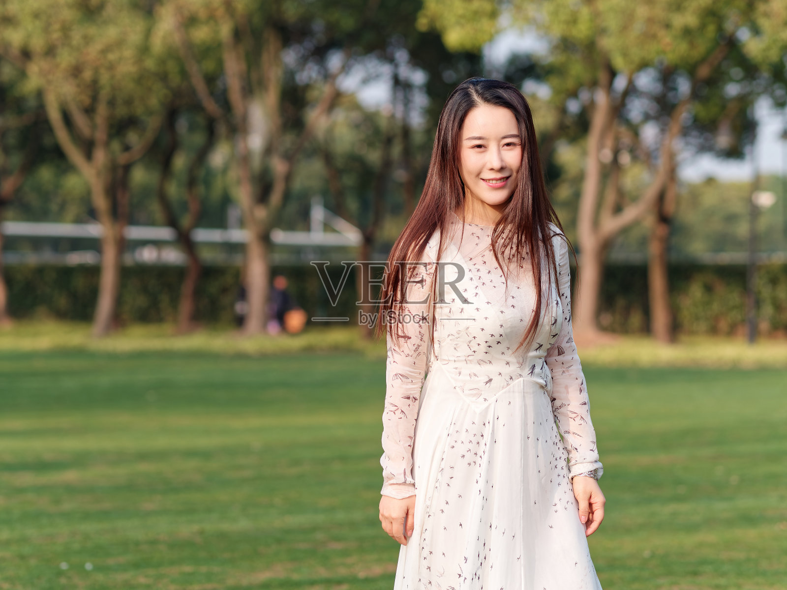 在阳光明媚的日子里，美丽的中国年轻女子穿着白衣，带着她闪亮的黑色长发微笑。照片摄影图片