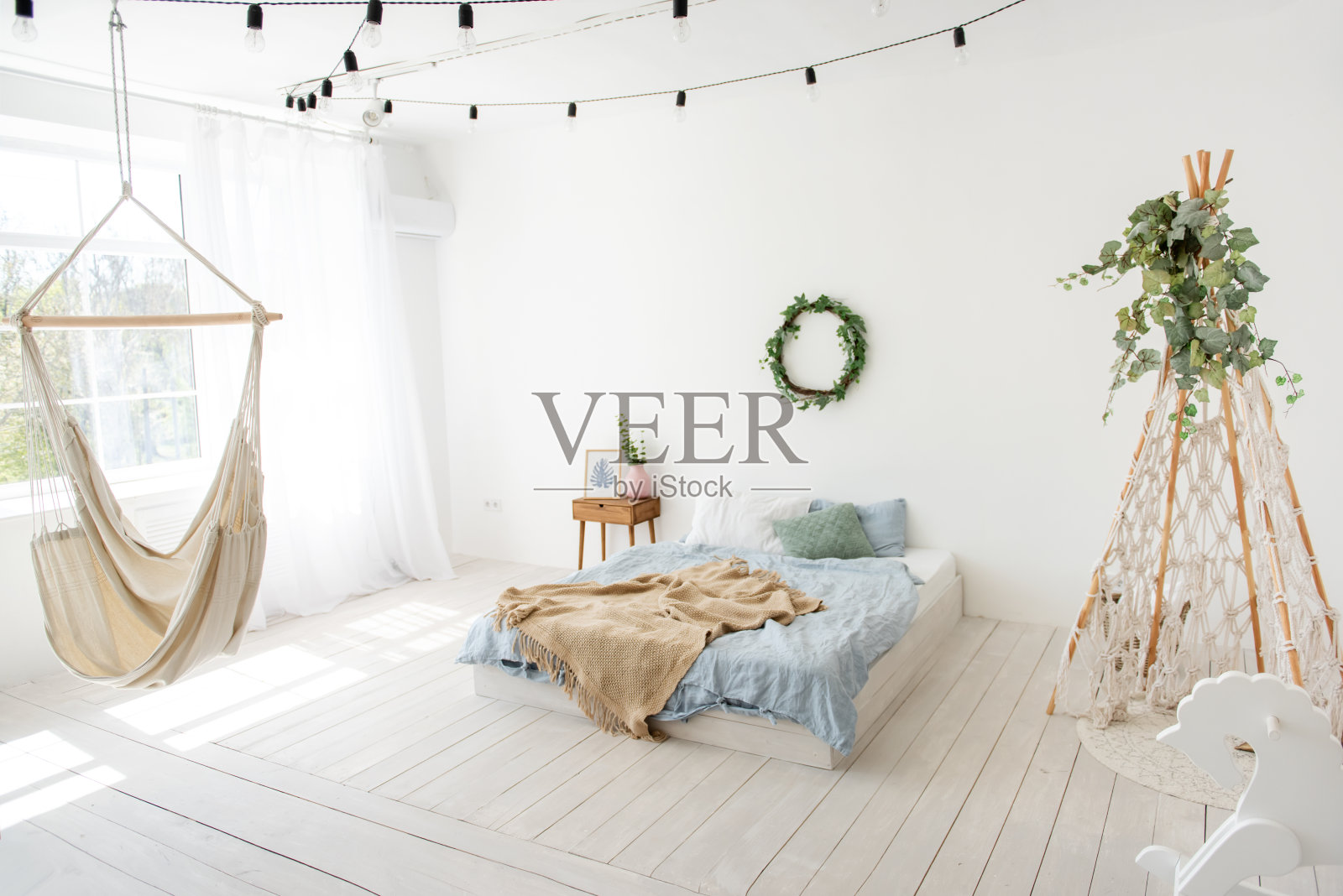 斯堪的纳维亚风格的时尚，时尚的室内。在白色的阁楼房间里，有绿色常春藤的wigwan流苏，地板上有床，木制摇木马，窗边挂着手工制作的吊床。本空间照片摄影图片