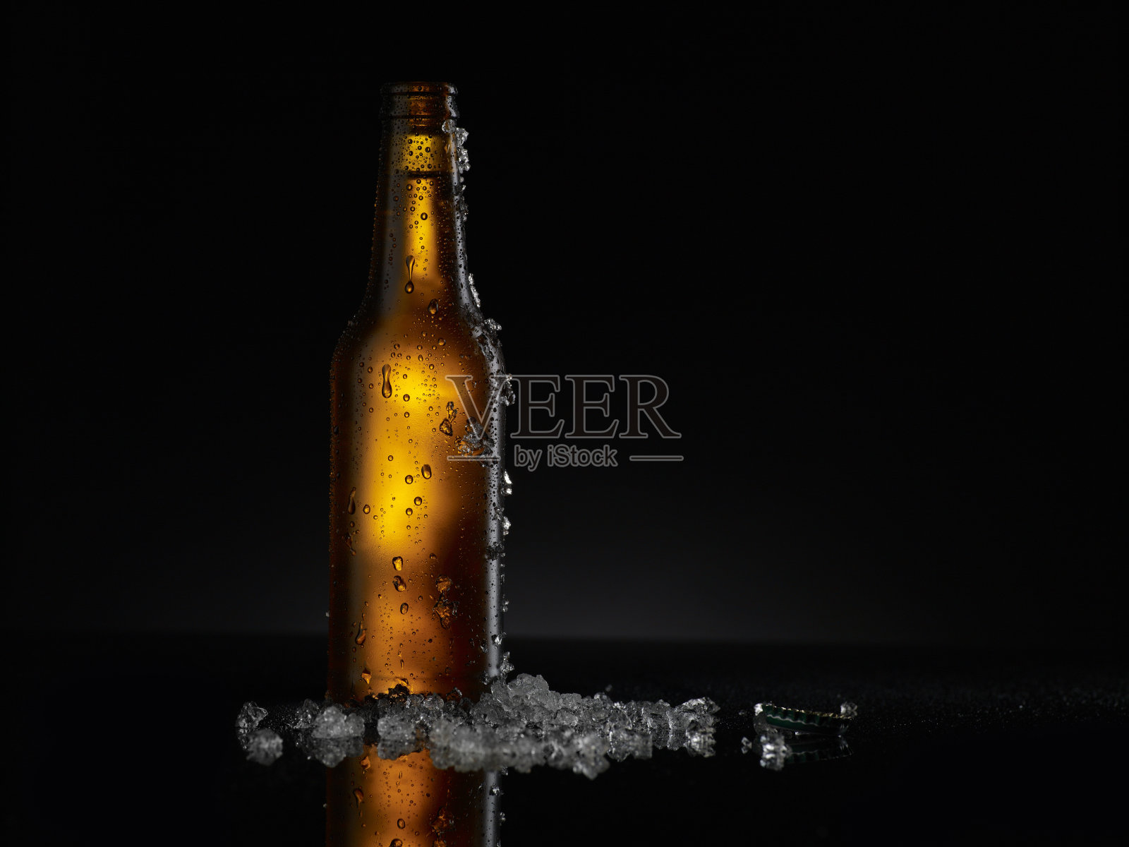 冰冷的棕色啤酒瓶上覆盖着冰和水滴-凝结。空白饮料饮料产品设计模型。站在黑色的桌子上，黑色的背景。照片摄影图片