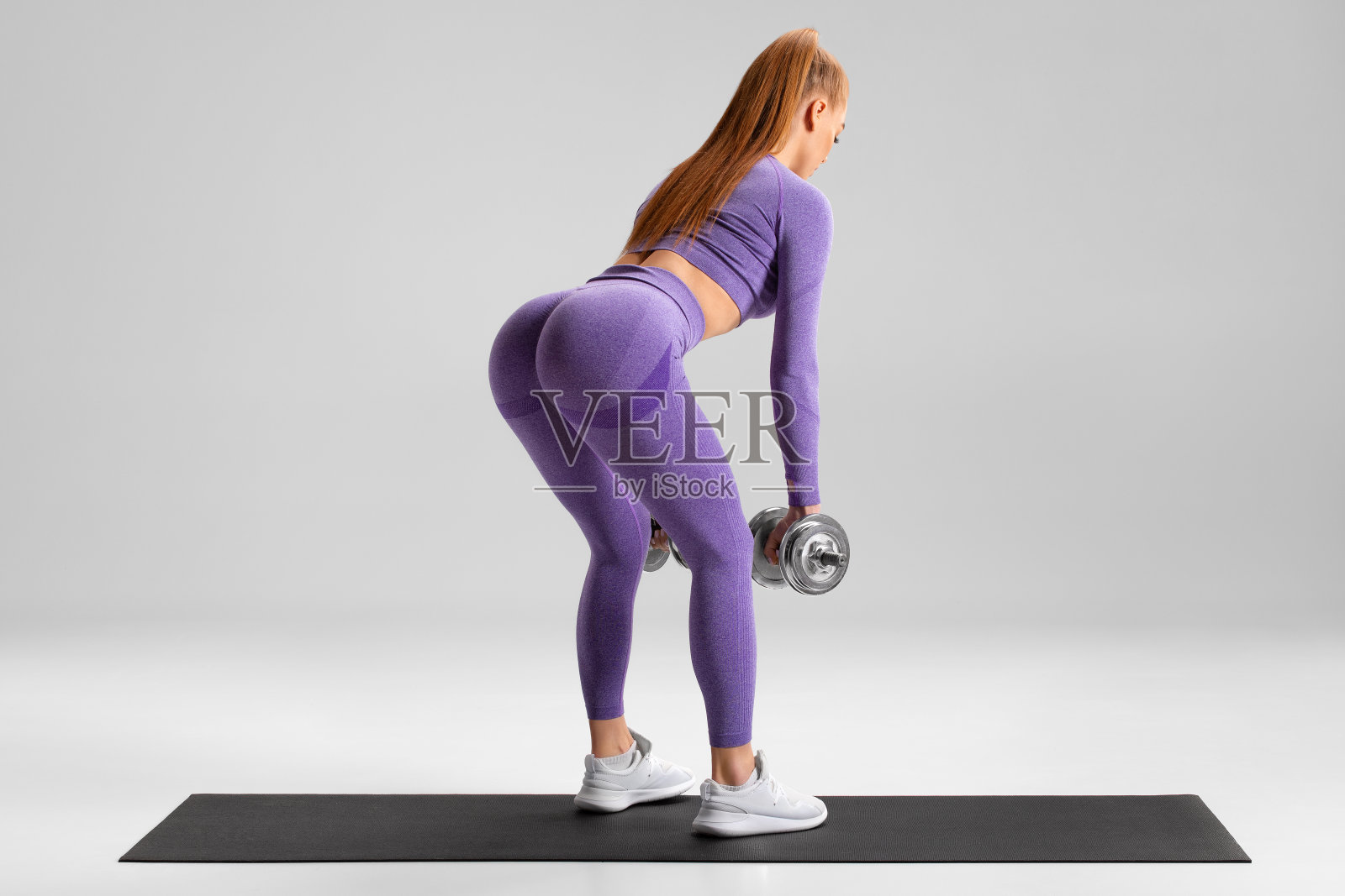 健身妇女做硬举运动的臀大肌在灰色的背景。运动女孩用哑铃锻炼照片摄影图片