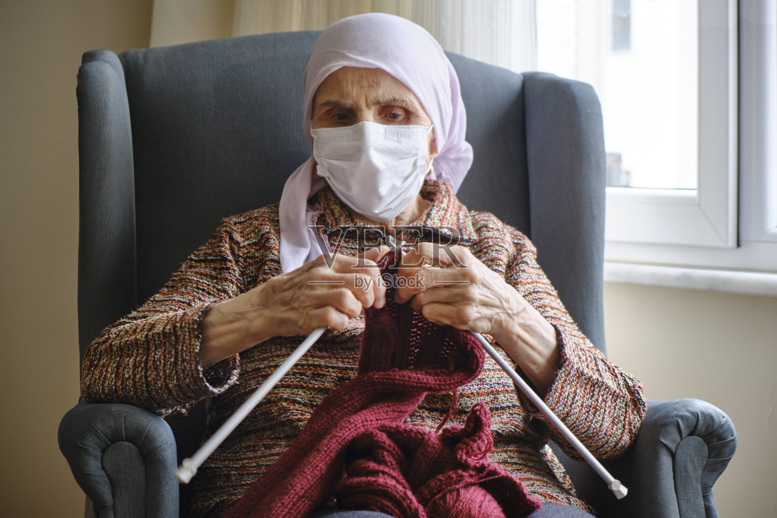 妇女编织一件毛衣与保护面罩在她的脸上照片摄影图片