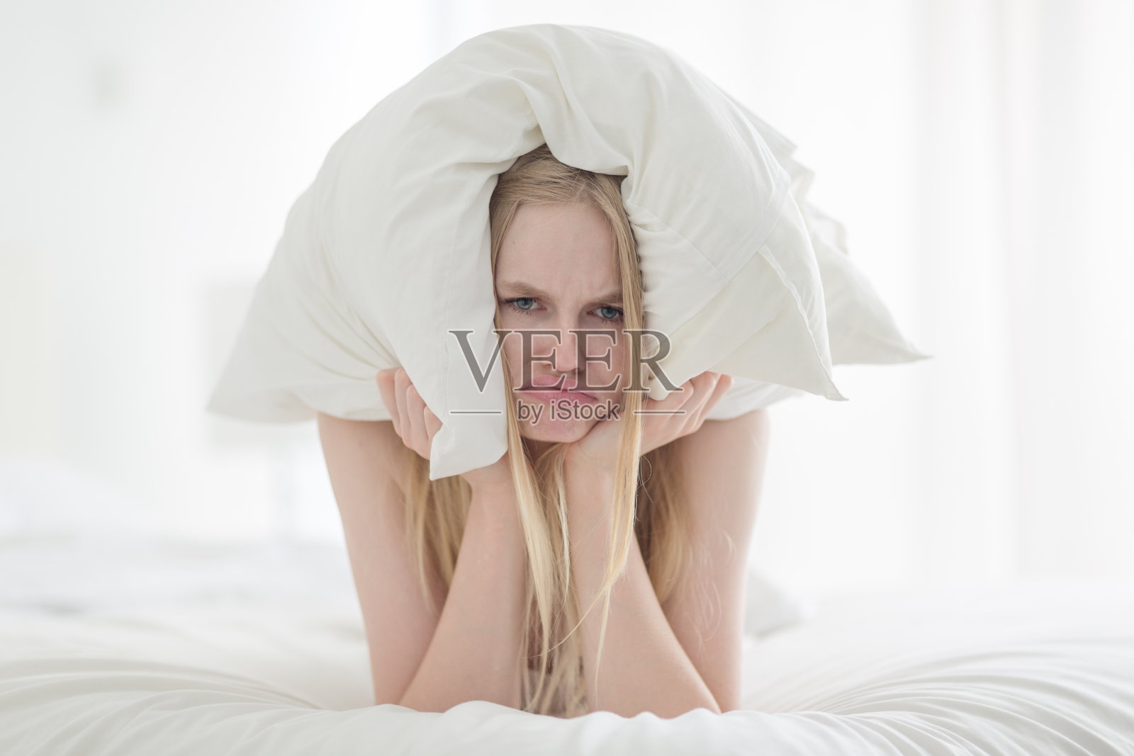 一个脾气暴躁的年轻女人用枕头捂住耳朵因为她床上太吵了。照片摄影图片