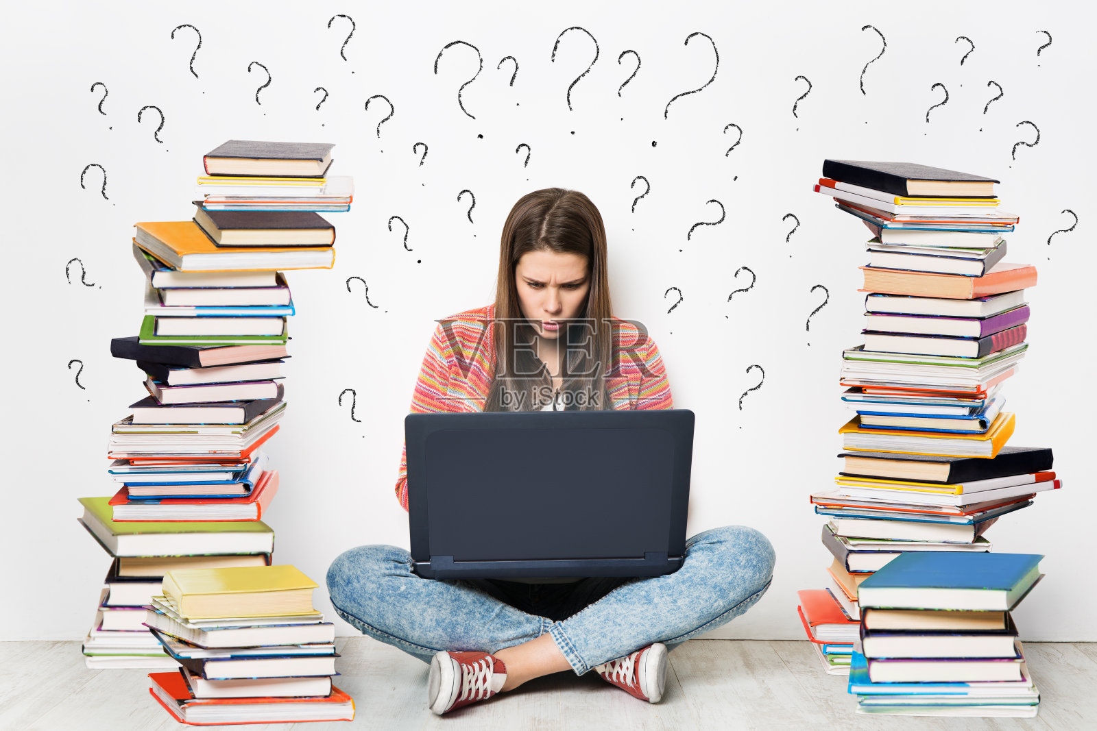 女人使用笔记本电脑。学生女孩在网上用电脑搜索成堆的书。白色墙壁背景上画的问号。电子学习、在线学习、数字图书馆图书阅读照片摄影图片