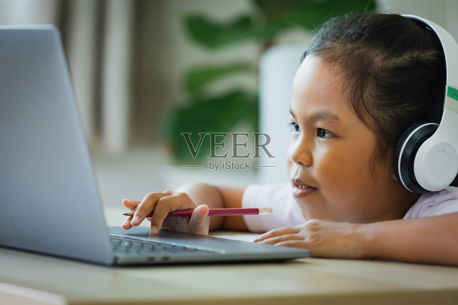 亚洲女童学生戴上耳机，通过视频电话与老师在线学习。由于Covid - 19大流行，在隔离期间，孩子正在用笔记本电脑在家学习。照片摄影图片