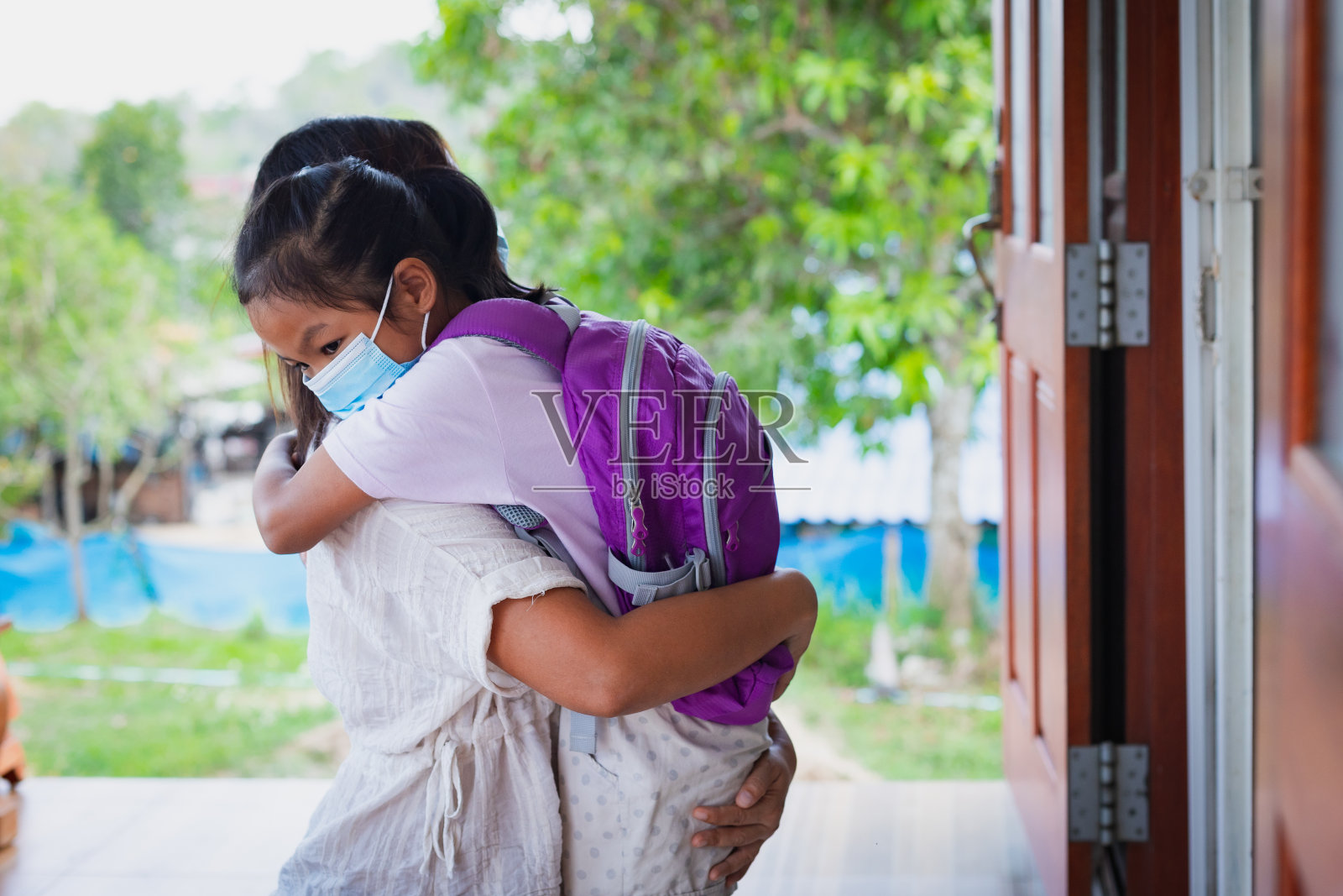 亚洲女童戴医用口罩防护COVID-19病毒爆发前拥抱母亲作为新的正常生活方式。照片摄影图片