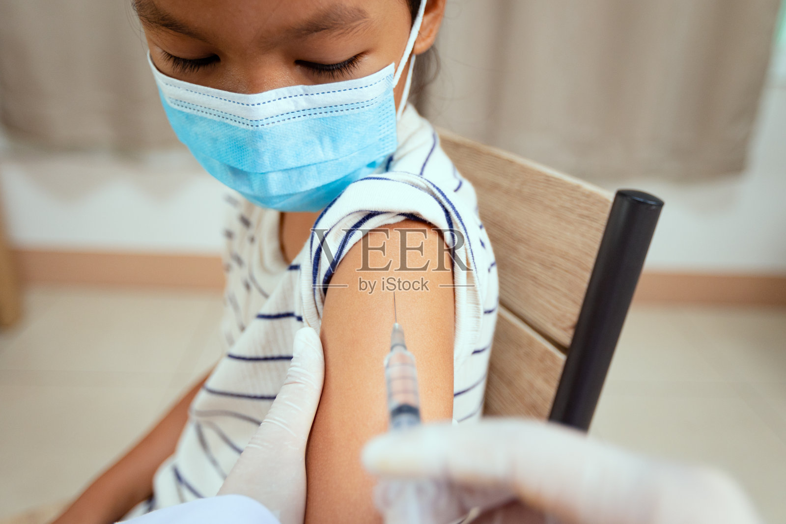 医生注射疫苗的亚洲儿童女孩的手臂。为保护新冠肺炎大流行佩戴防护口罩的女童。照片摄影图片