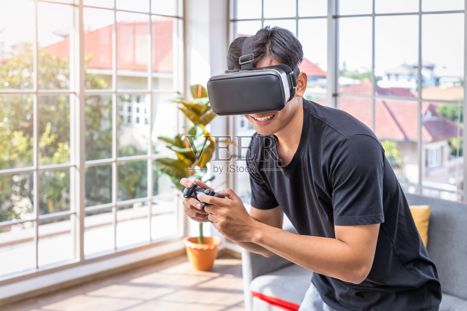 年轻的亚洲男子戴着虚拟现实VR头戴眼镜，手持控制器玩着未来游戏照片摄影图片