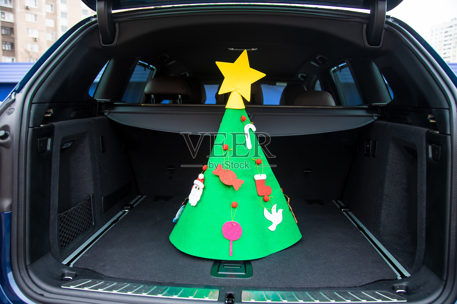 新年假期旅游。一棵装饰着玩具和星星的毛线圣诞树矗立在一辆现代跨界车的空树干的中央。特写,软焦点照片摄影图片