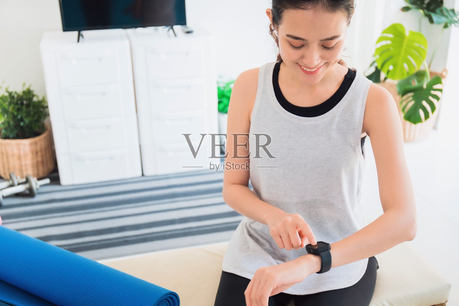 亚洲女性休息和使用智能手表后玩瑜伽和锻炼在家里的背景与拷贝空间。运动技术的概念来检查健康数据。照片摄影图片