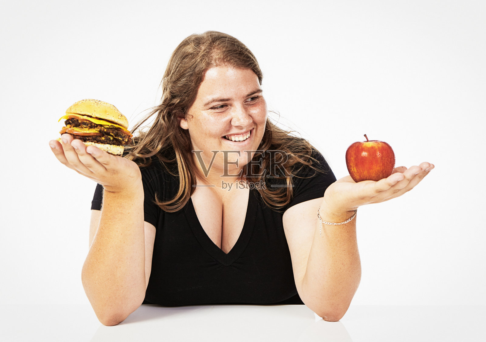 一个快乐的年轻女人拿着一个红苹果和一个汉堡，在健康和不健康的饮食中选择照片摄影图片