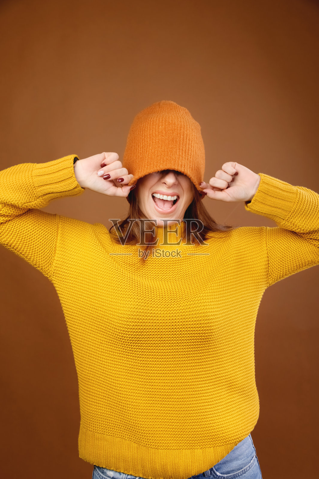 一个快乐的女孩的肖像，浅棕色的长发有乐趣，用一个大的针织套索帽遮住她的眼睛，微笑着，穿着黄色毛衣完美的白牙齿照片摄影图片