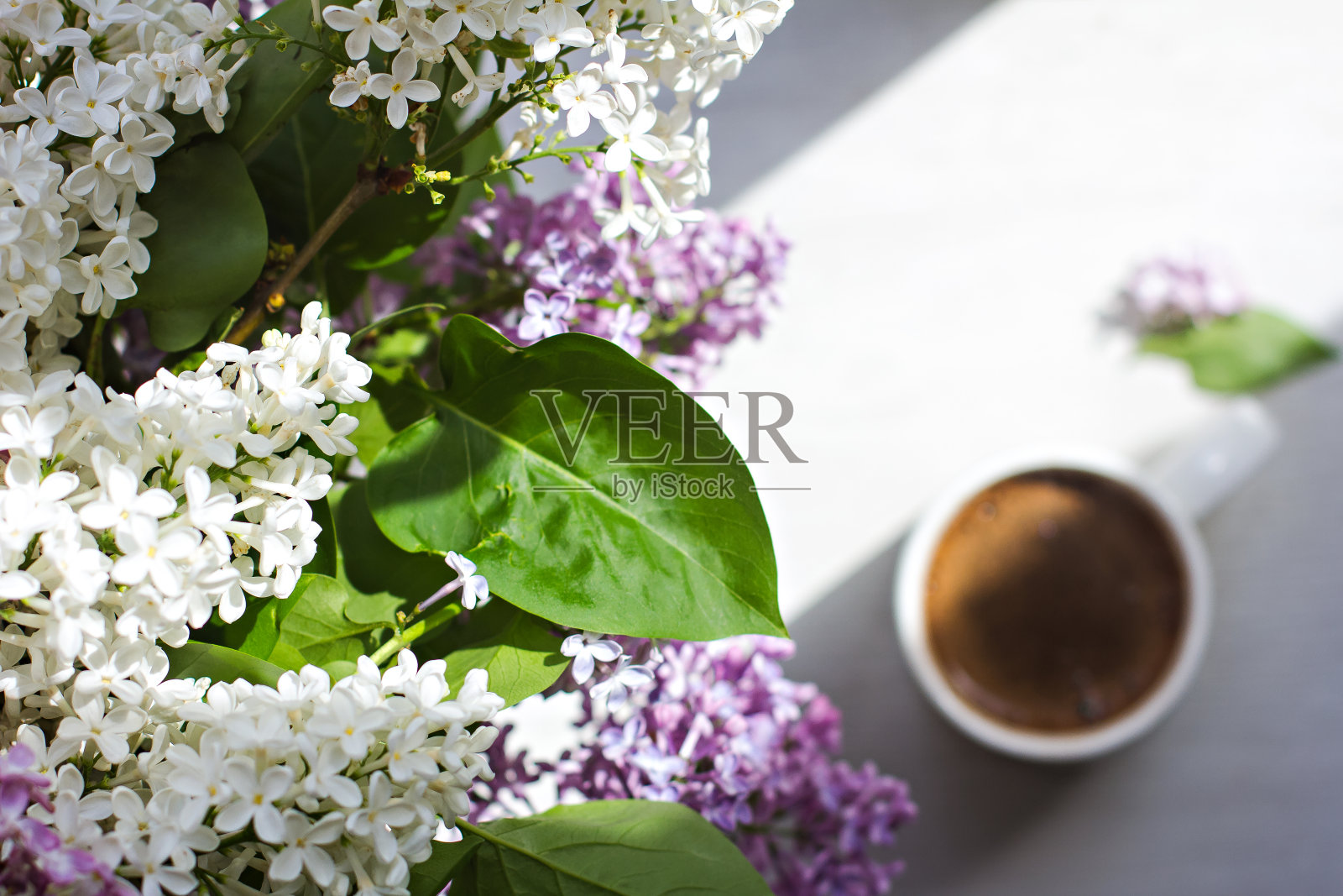 窗户上一束花，阳光下白色杯子里的咖啡。一束紫丁香和一杯咖啡。照片摄影图片