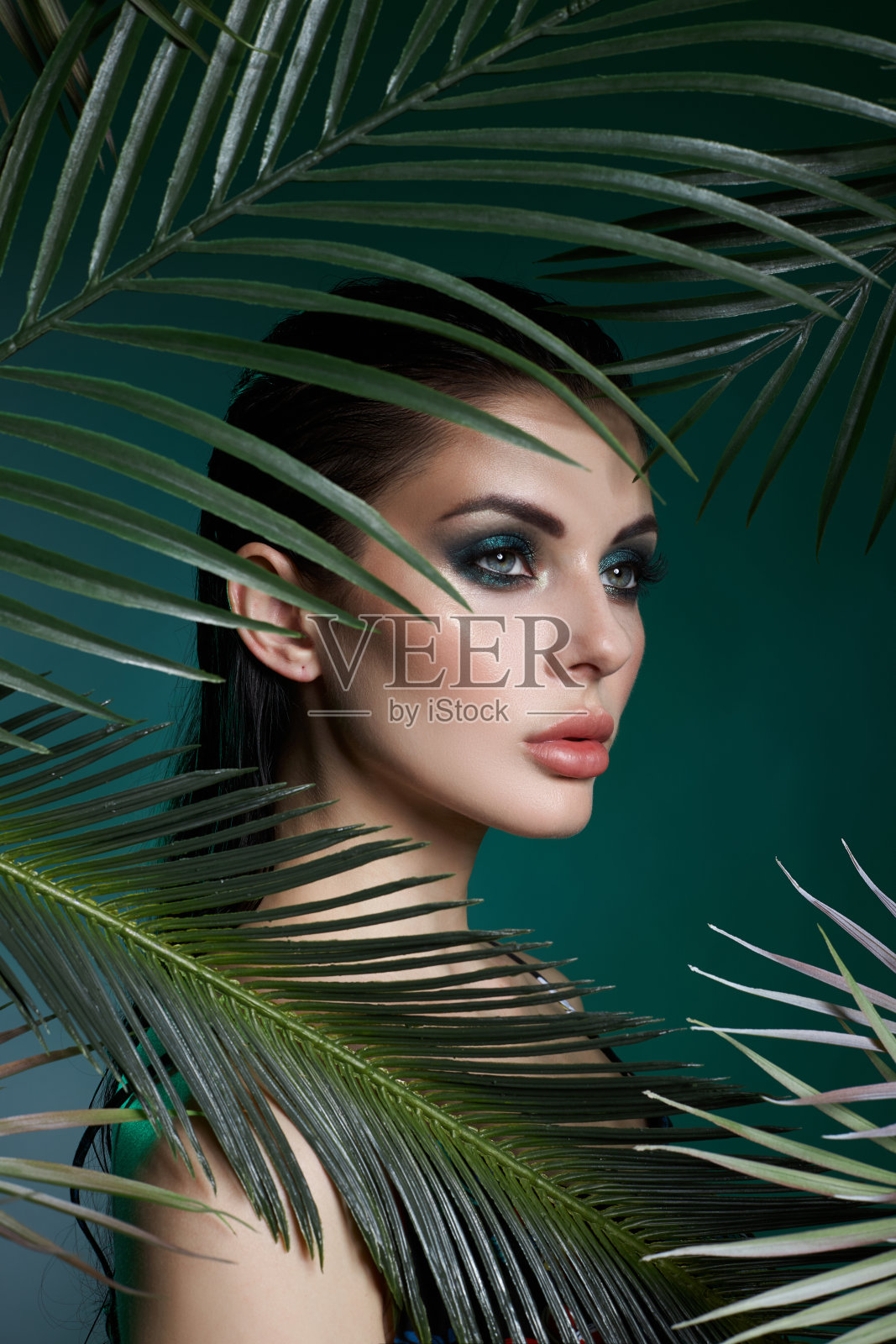 热带肖像性感的女人在树叶棕榈树。亮绿色的妆，少女脸上棕榈叶的阴影。美丽的妆照片摄影图片