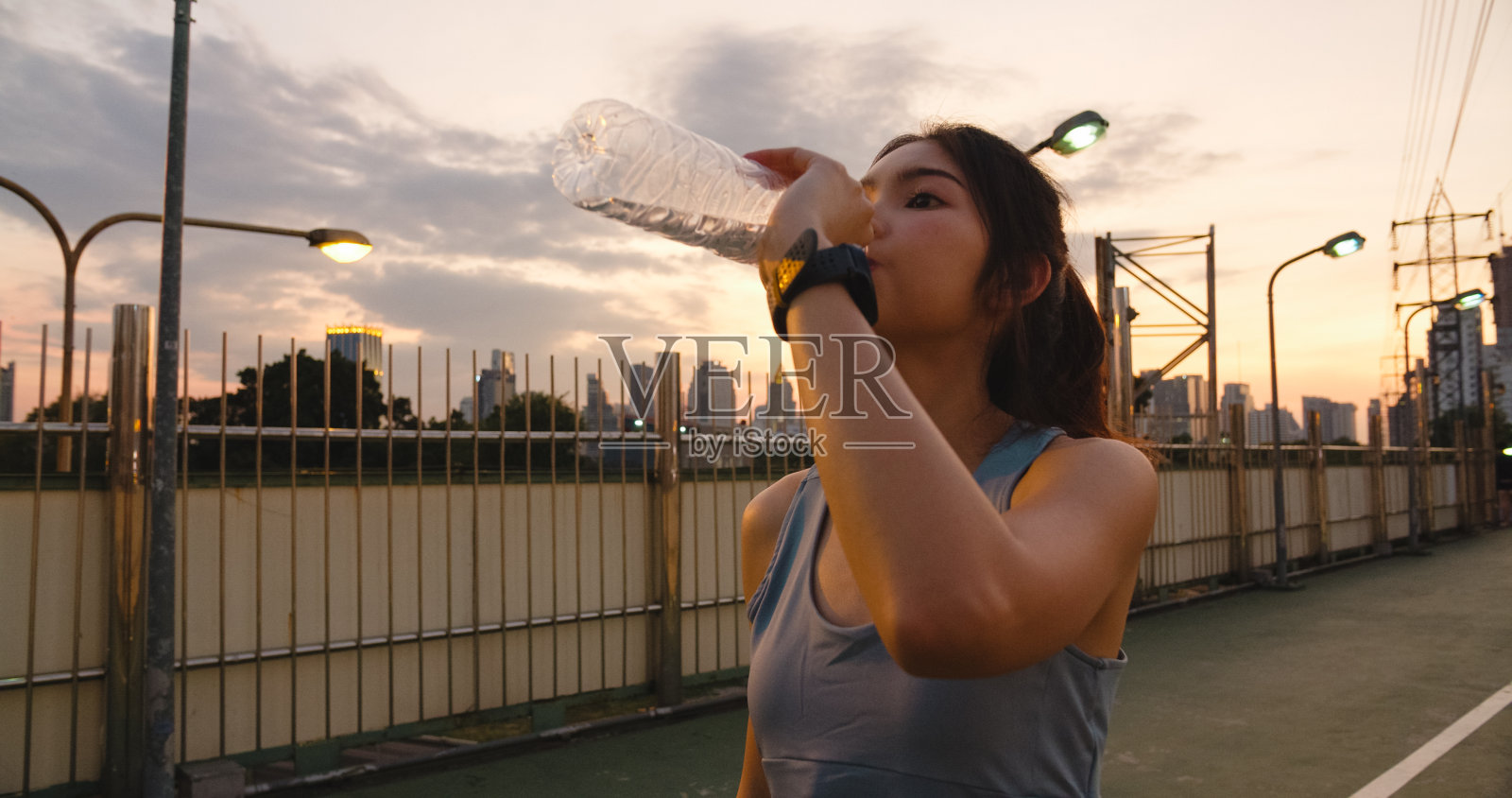 美丽的年轻亚洲运动员女士锻炼喝水是因为在城市环境中跑步后感到疲劳。照片摄影图片