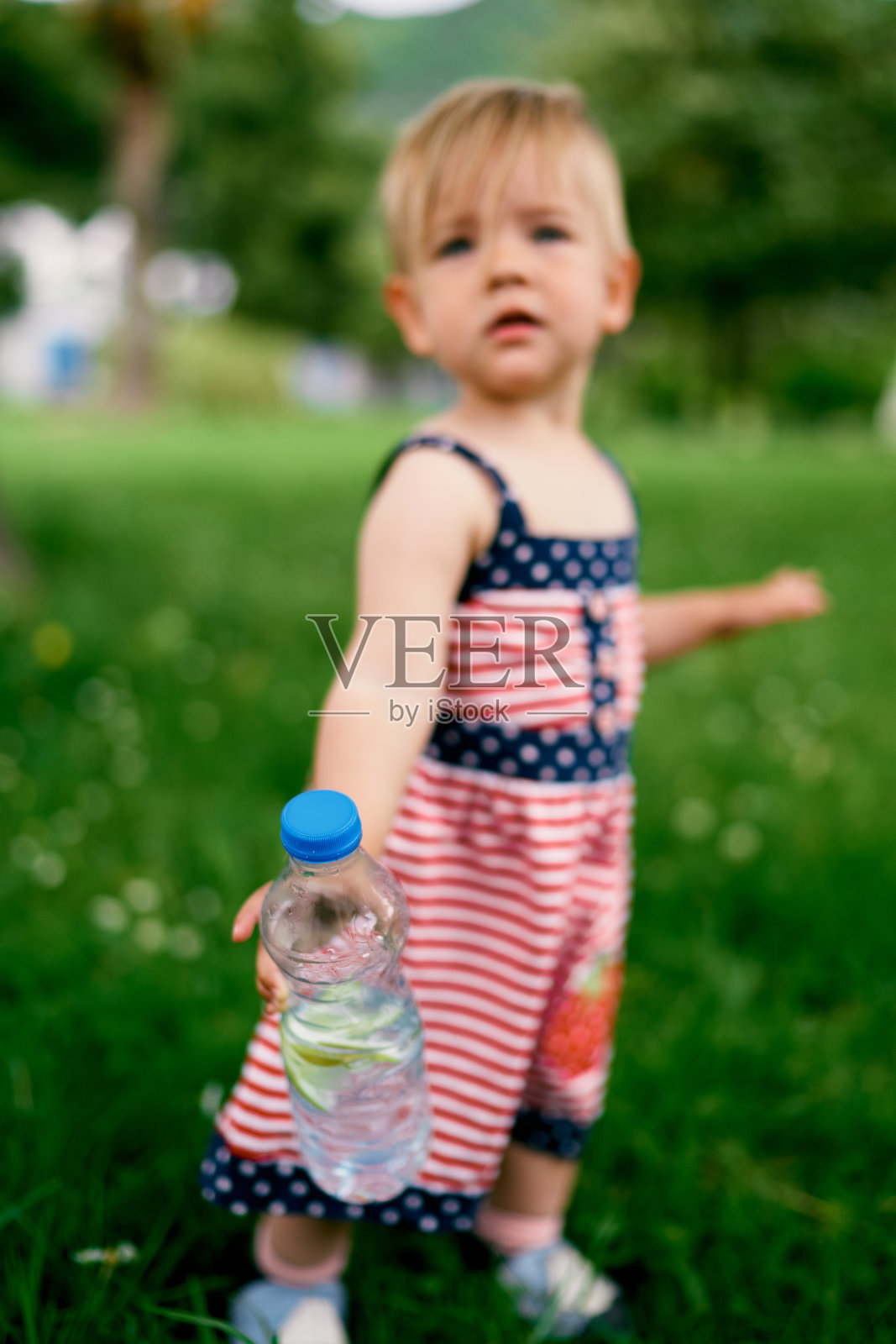 小女孩站在绿色的草坪上，手里拿着一个装着水的塑料瓶照片摄影图片