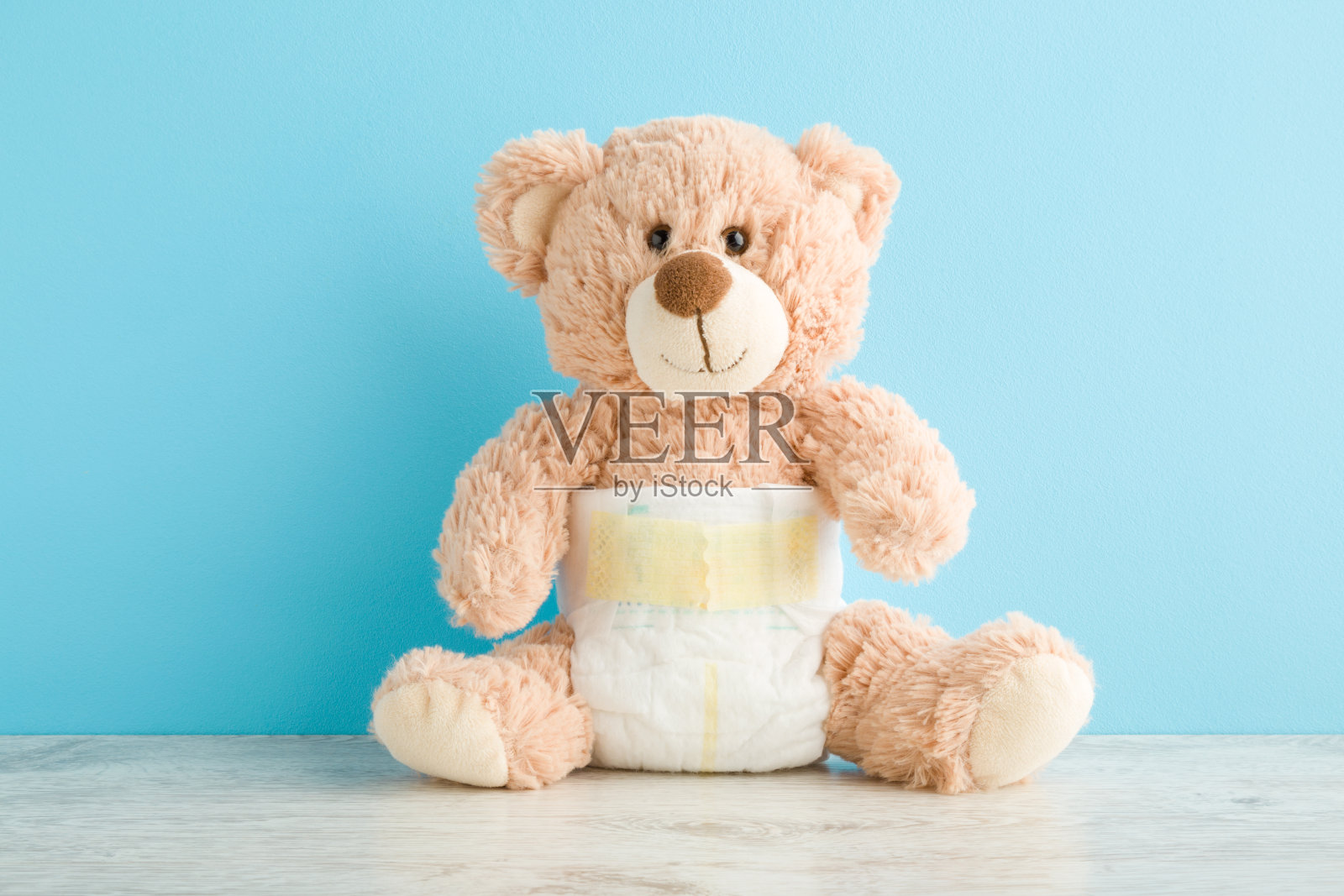 棕色的泰迪熊在白色柔软的婴儿尿布在浅蓝色的墙壁背景桌上。柔和的颜色。特写镜头。前视图。照片摄影图片
