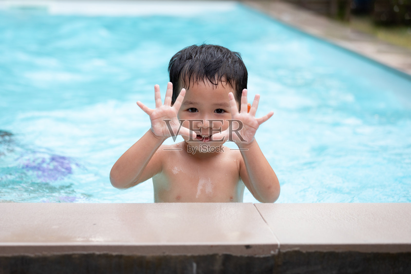 亚洲小男孩在游泳池里玩水时，看着镜头微笑。照片摄影图片