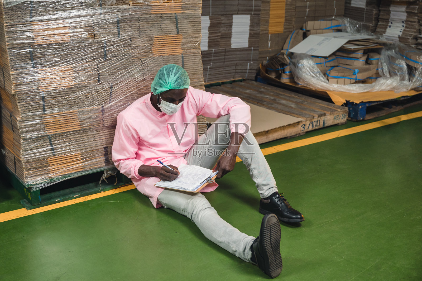 库存控制经理非洲男穿着无菌制服坐在仓库检查顺序纸箱包装堆放在仓库照片摄影图片