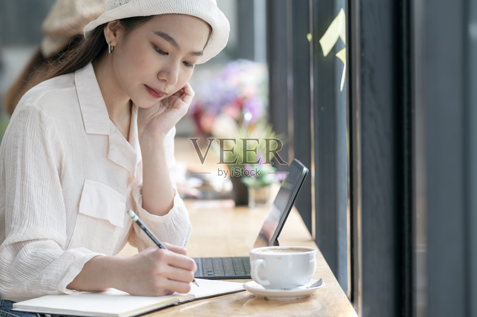 近距离观察年轻的亚洲女人思考和书写笔记本，而坐在柜台在共同工作空间。照片摄影图片