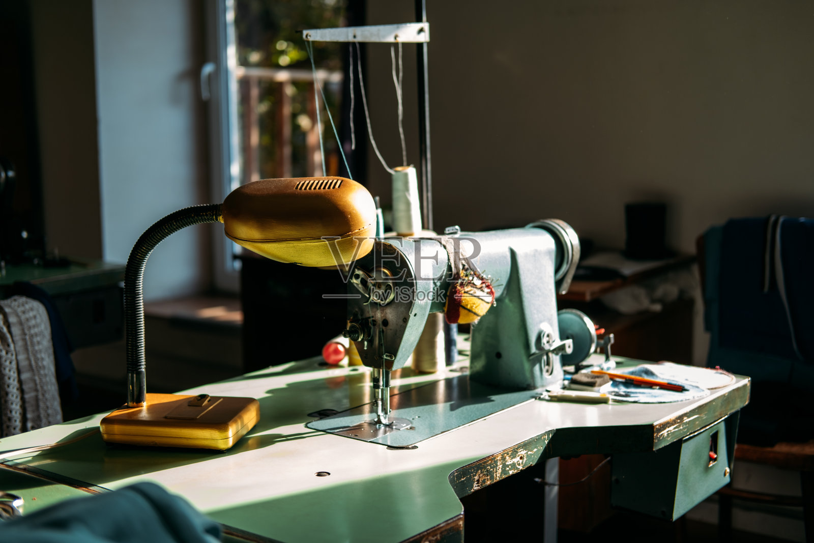 在阳光下，缝纫机放在工厂的桌子上。小型企业，时装设计，裁缝工作，坦诚的裁缝工作场所，服装或服装行业照片摄影图片