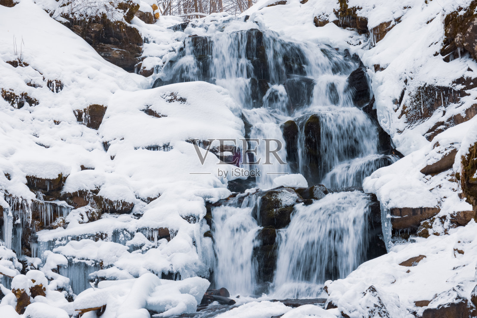 小瀑布般的凉水在白雪覆盖的石头间流动照片摄影图片