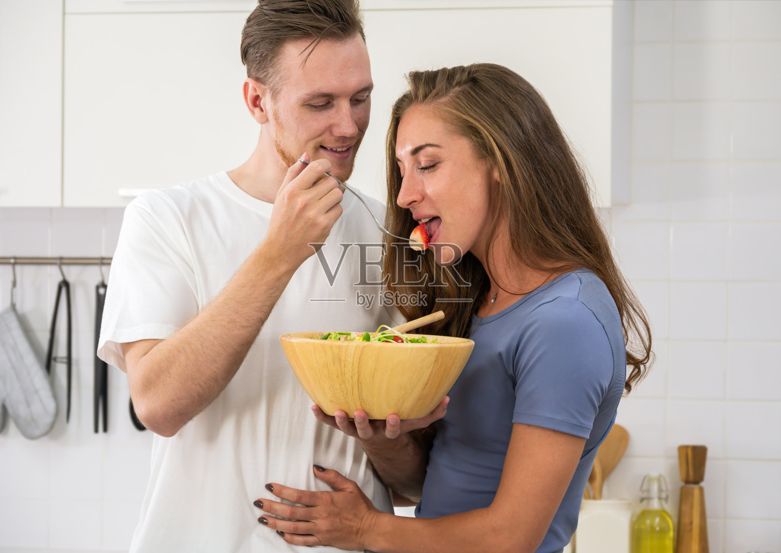 一对快乐的夫妇在家里的厨房里一起吃沙拉照片摄影图片