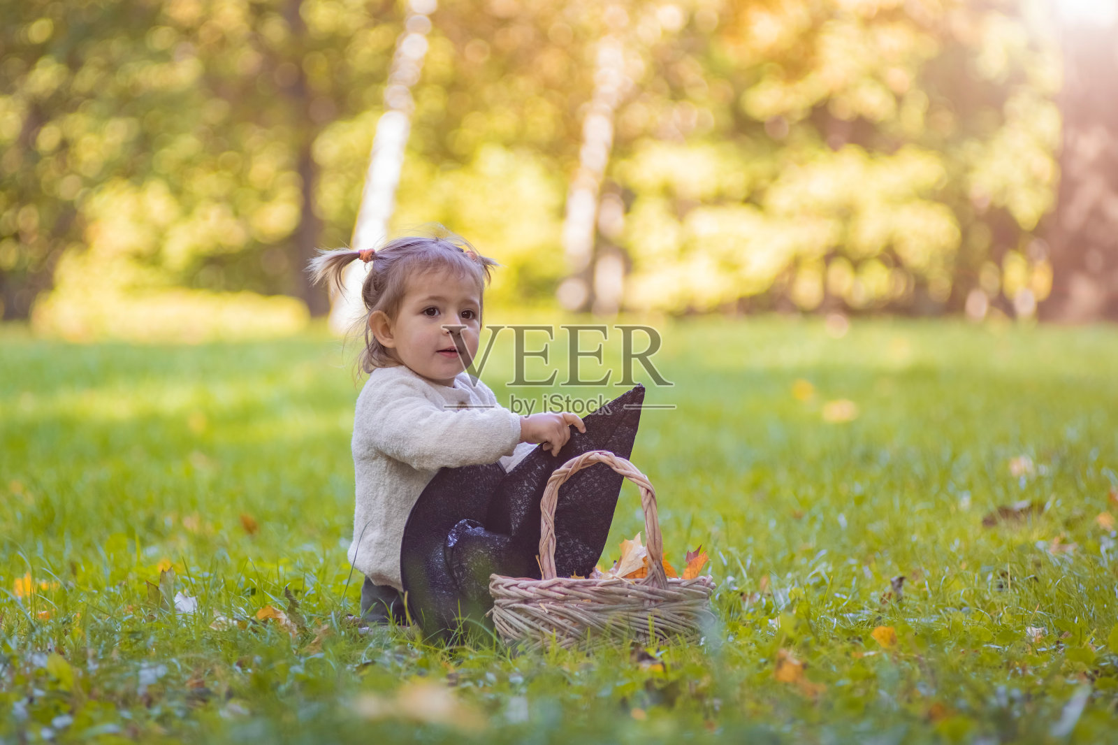 蹒跚学步的孩子在秋天阳光明媚的公园玩女巫帽。照片摄影图片