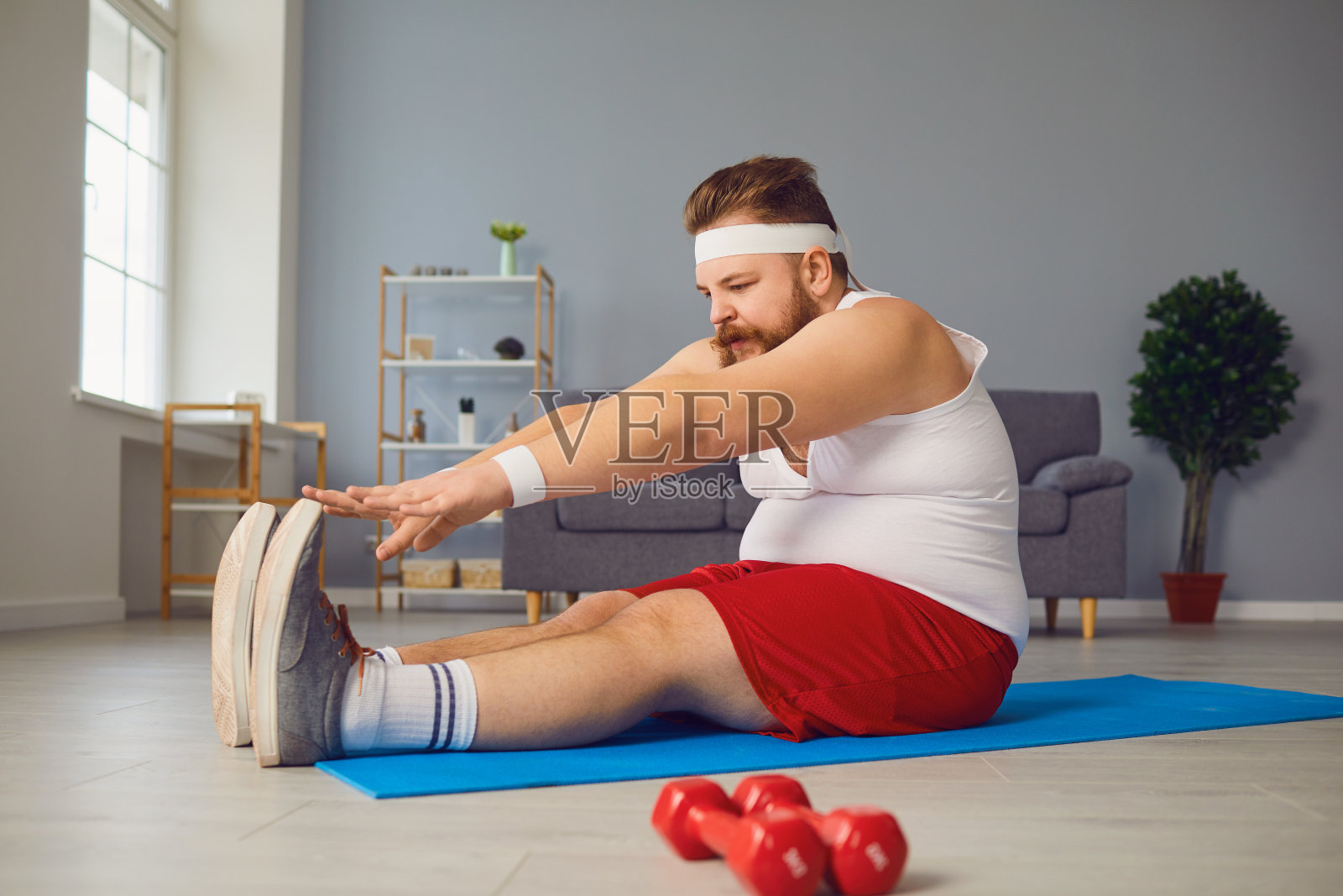 滑稽的红胖子站在家里的地板上做运动。照片摄影图片