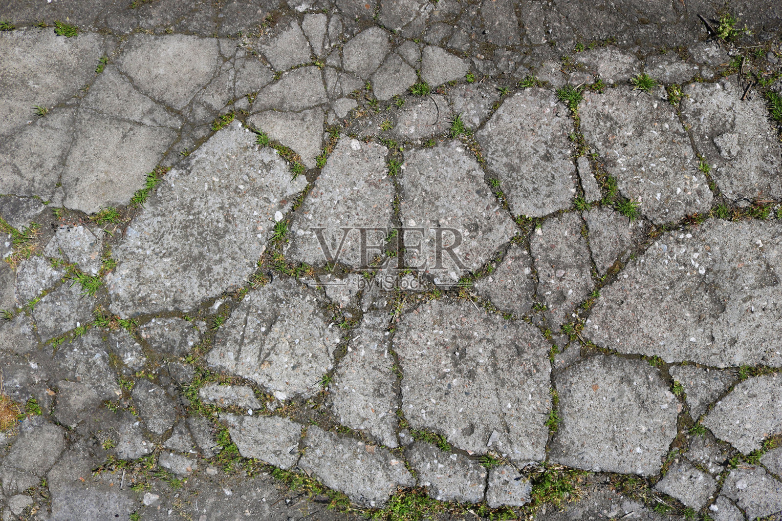 破碎和开裂的水泥表面从地面与不规则的形状和形态和草之间的碎片-特写粗糙的纹理图案照片摄影图片