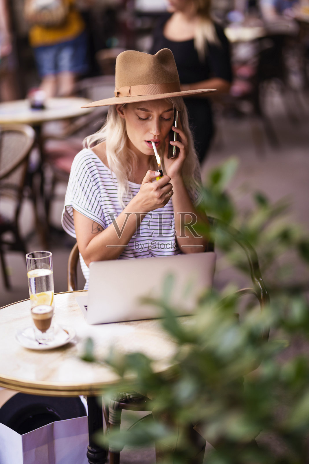 年轻女子一边抽烟一边用手机坐在户外咖啡馆照片摄影图片