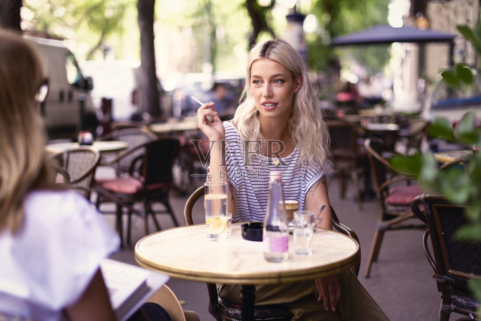 年轻的金发女人坐在露天咖啡馆里抽着烟照片摄影图片