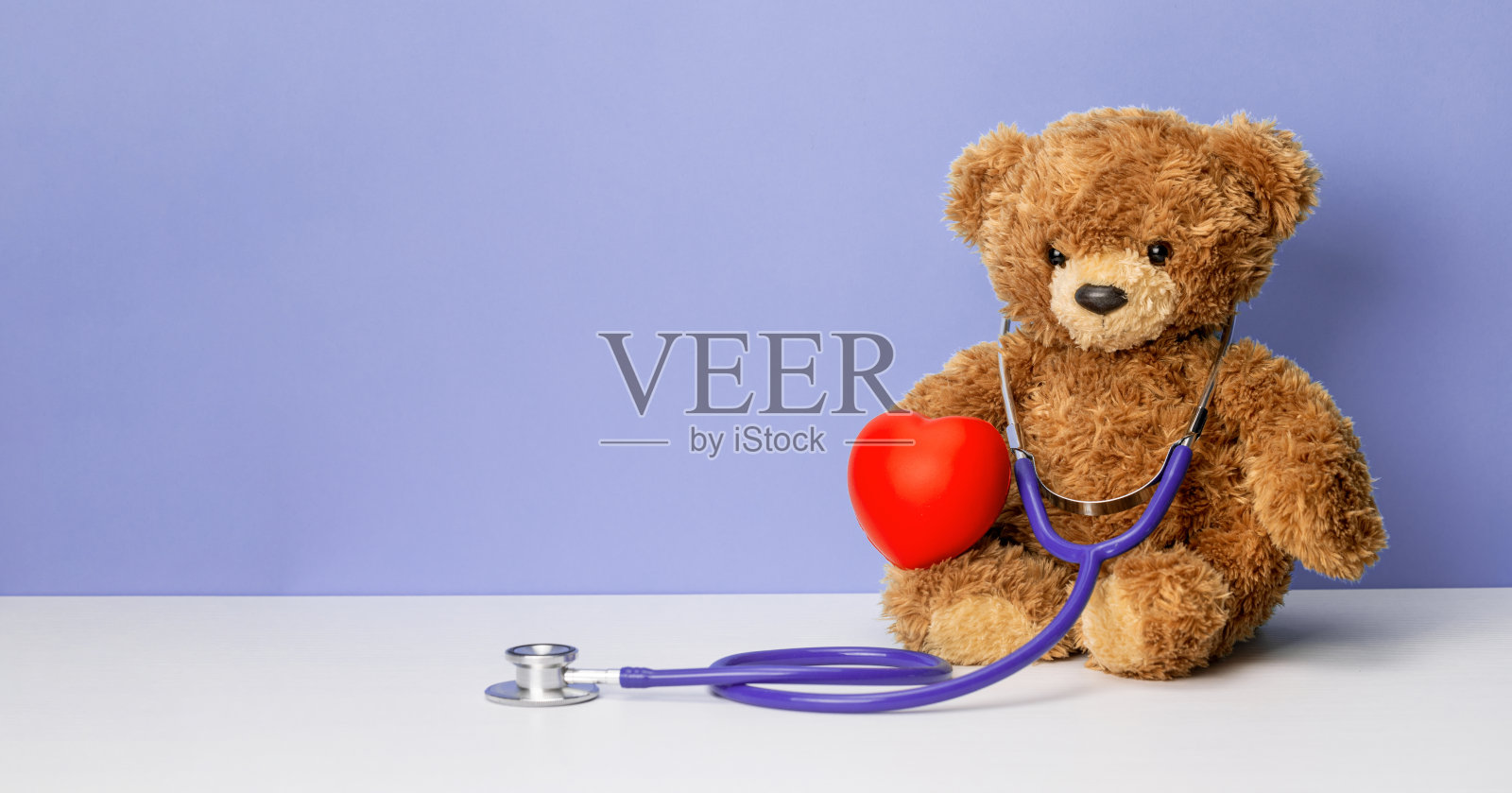 泰迪熊，带着听诊器，紫色背景上有颗心。家庭医生或儿科医生的概念照片摄影图片
