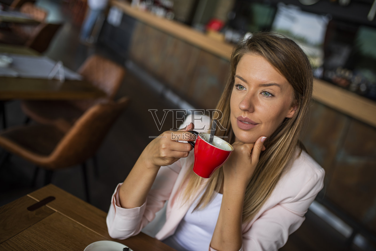 一个沉思的女人坐在自助餐厅里，拿着咖啡杯，却看向别处。照片摄影图片