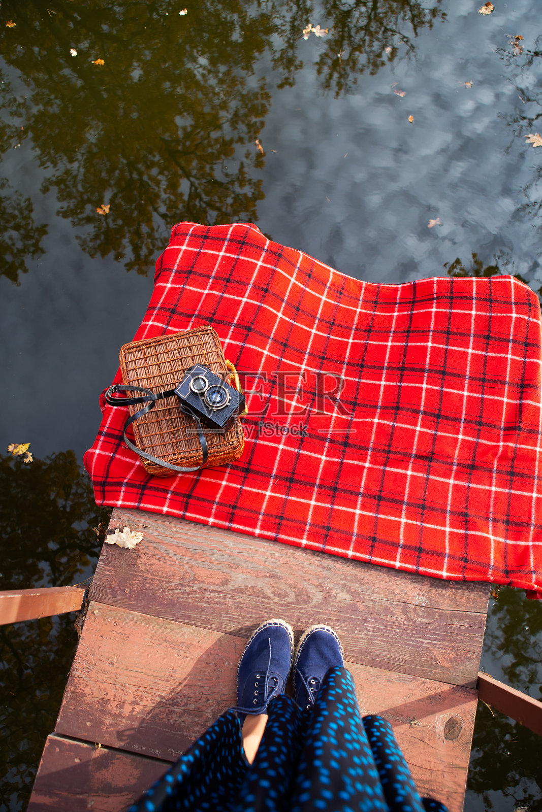 那架旧照相机放在红格子布上的手提箱上。湖边的木桥。照片里女孩的腿。照片摄影图片