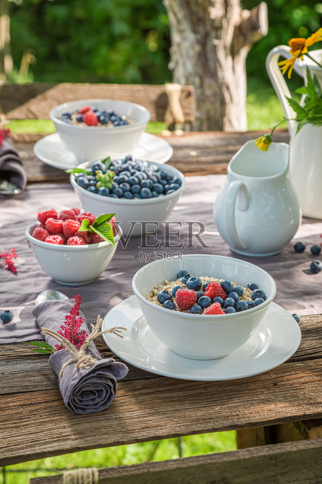 新鲜早餐，有浆果和牛奶。在阳光明媚的花园里吃饭。照片摄影图片