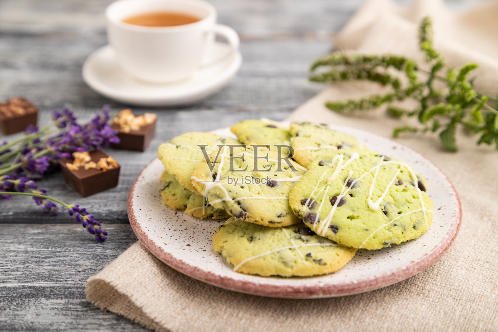绿色饼干，巧克力和薄荷放在陶瓷盘子和一杯绿茶和亚麻纺织品在灰色木制背景。侧视图，特写，选择性聚焦。照片摄影图片