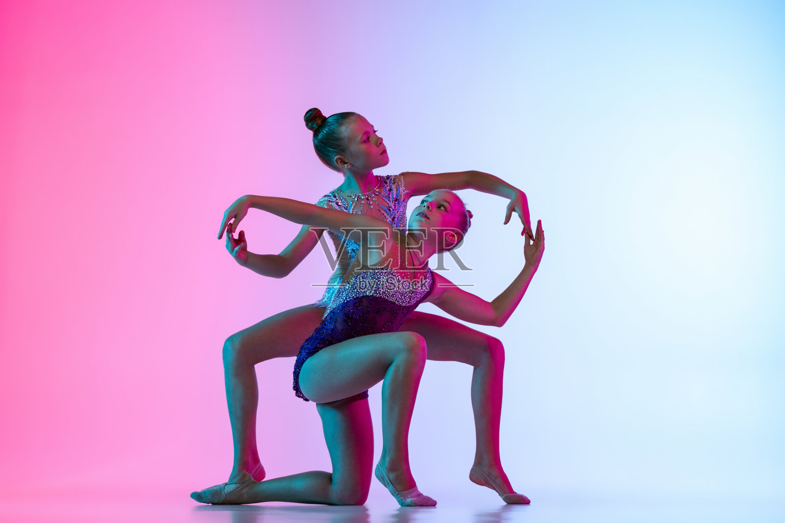 两个小美丽的艺术体操艺术家的肖像，女孩在体育事件孤立在梯度粉红色的蓝色工作室背景在霓虹灯照片摄影图片